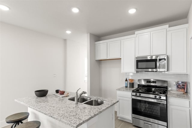 kitchen featuring appliances with stainless steel finishes, a sink, white cabinets, backsplash, and a breakfast bar area