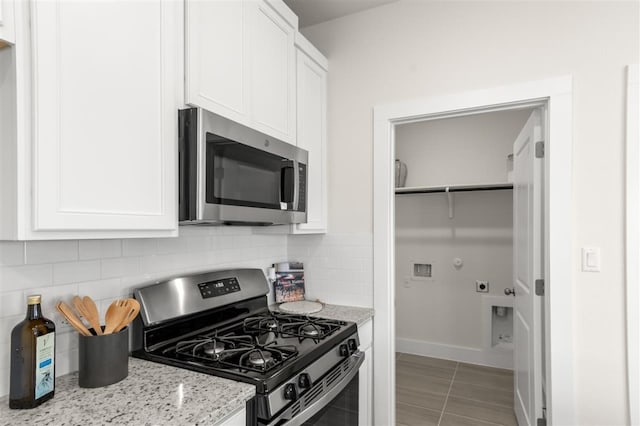 kitchen featuring appliances with stainless steel finishes, white cabinetry, decorative backsplash, light stone countertops, and baseboards