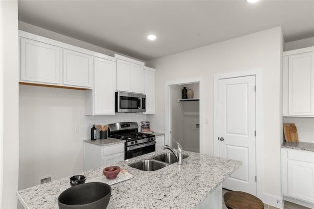 kitchen featuring appliances with stainless steel finishes, a sink, white cabinetry, light stone countertops, and recessed lighting