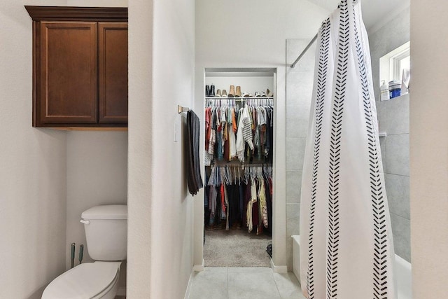 bathroom with toilet, shower / bathtub combination with curtain, a walk in closet, and tile patterned flooring