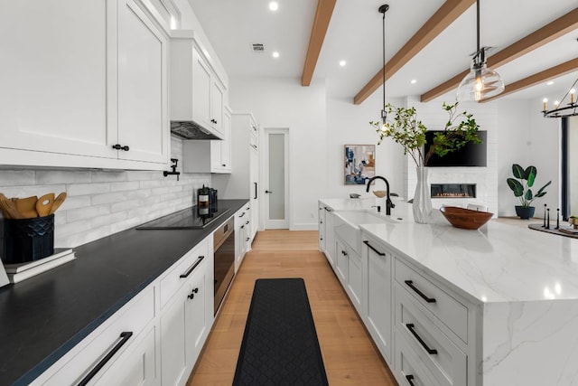 13408 Galleria Cir, Austin, TX 78738 - kitchen featuring tasteful backsplash, white cabinetry, black electric stovetop, beam ceiling, and a glass covered fireplace