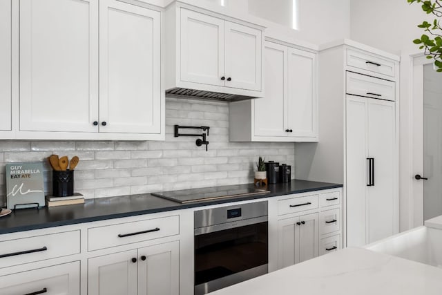 13408 Galleria Cir, Austin, TX 78738 - kitchen featuring wall oven, black electric stovetop, backsplash, and white cabinets