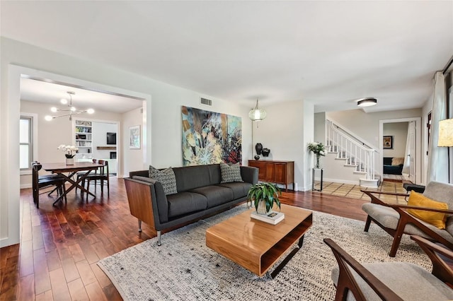 living area featuring stairway, dark wood-type flooring, baseboards, and a chandelier