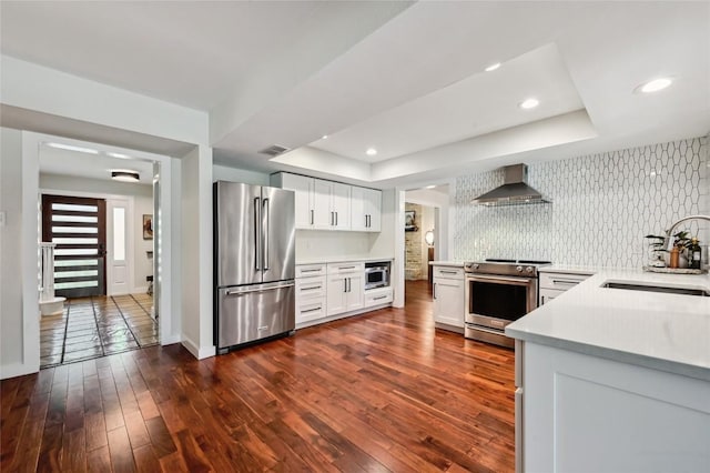 kitchen with appliances with stainless steel finishes, wall chimney range hood, a sink, a tray ceiling, and light countertops