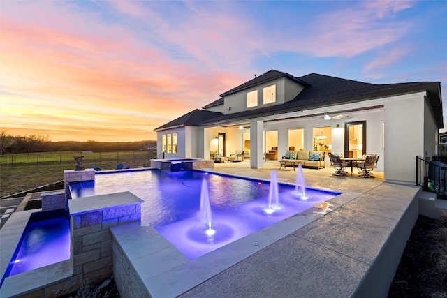 back of property with a fenced backyard, a pool with connected hot tub, a patio, stucco siding, and an outdoor living space