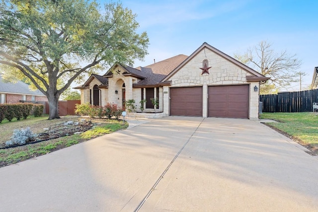 ranch-style home with concrete driveway, stone siding, an attached garage, and fence