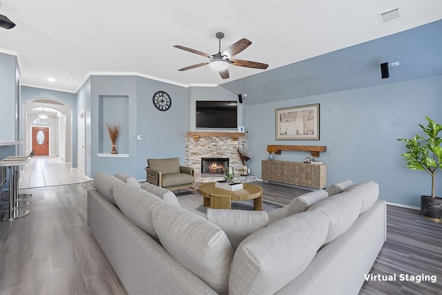 living area with a ceiling fan, a stone fireplace, baseboards, arched walkways, and wood finished floors