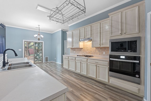 kitchen featuring light wood-style flooring, stainless steel appliances, light countertops, ornamental molding, and a sink