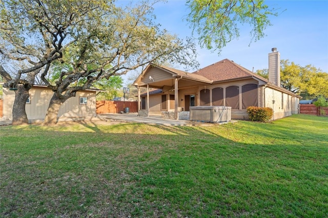 rear view of property with a patio, a yard, a fenced backyard, a hot tub, and a chimney