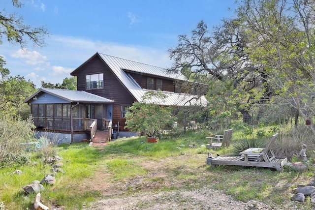 rear view of property featuring a wooden deck, metal roof, and a sunroom