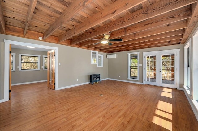 unfurnished living room with a wood stove, a wall unit AC, beam ceiling, and french doors