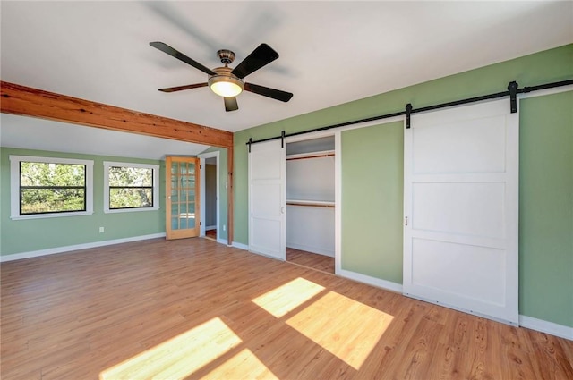 unfurnished bedroom with beamed ceiling, light wood-style flooring, a barn door, and baseboards