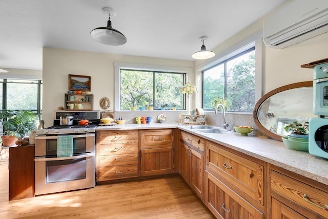 kitchen featuring double oven range, light wood-style flooring, a sink, light countertops, and an AC wall unit