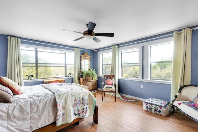 bedroom featuring wood finished floors, ceiling fan, baseboards, and multiple windows