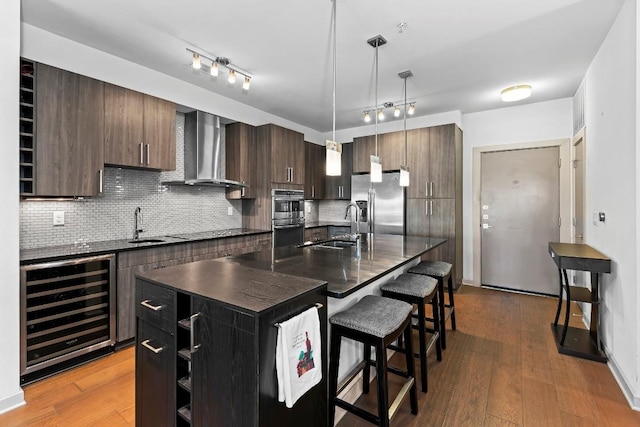 3600 S Lamar Blvd Unit 211, Austin, TX 78704 - kitchen featuring wine cooler, a breakfast bar area, wall chimney exhaust hood, dark countertops, and appliances with stainless steel finishes