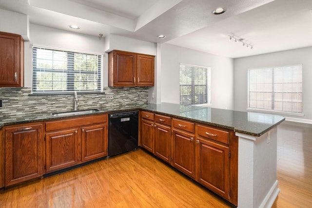 1704 W Ave Unit 108, Austin, TX 78701 - kitchen with black dishwasher, a sink, a peninsula, light wood-style floors, and dark stone counters