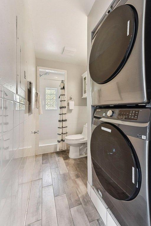 7067 Comanche Trl, Austin, TX 78732 - bathroom with stacked washer and clothes dryer, tile walls, toilet, wood finished floors, and curtained shower