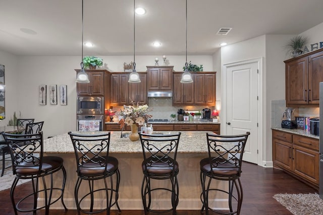2429 Carretera Dr, Leander, TX 78641 - kitchen with under cabinet range hood, tasteful backsplash, a center island with sink, dark wood-type flooring, and recessed lighting