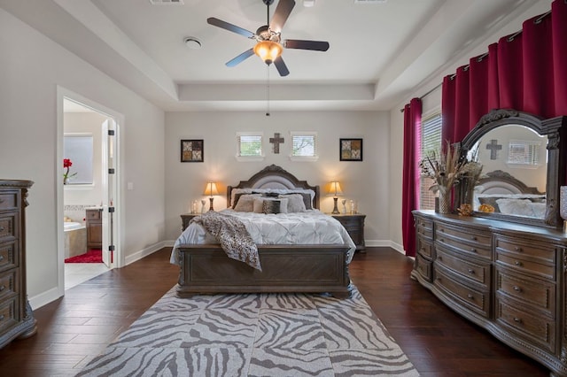 2429 Carretera Dr, Leander, TX 78641 - bedroom with dark wood-type flooring, a tray ceiling, baseboards, ensuite bathroom, and a ceiling fan
