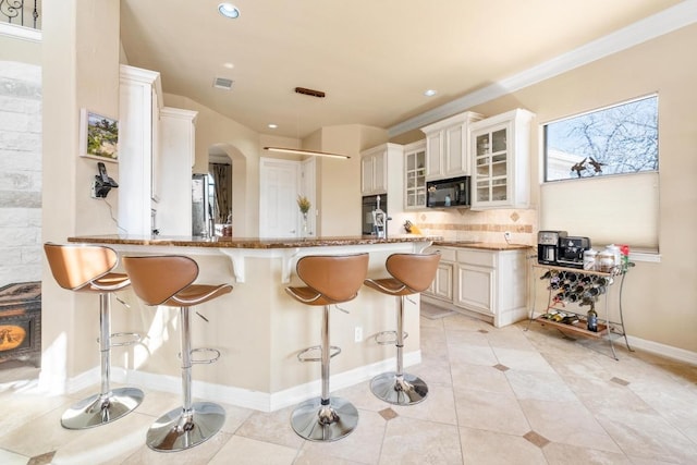 329 Park Place Dr, Georgetown, TX 78628 - kitchen with black microwave, arched walkways, a kitchen bar, fridge, and backsplash