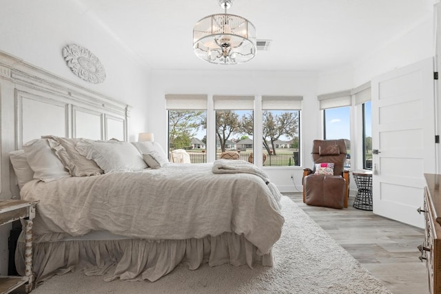 bedroom with a chandelier, light wood-type flooring, multiple windows, and visible vents