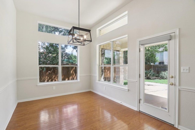 unfurnished dining area with a chandelier, hardwood / wood-style floors, and baseboards