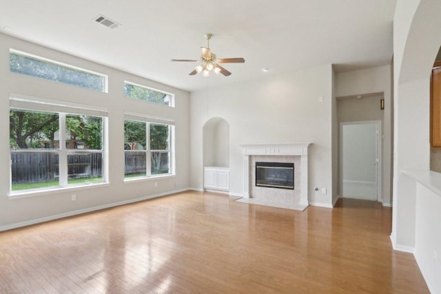 unfurnished living room with a ceiling fan, wood finished floors, a tile fireplace, and baseboards