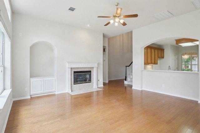 unfurnished living room featuring wood finished floors, a ceiling fan, a fireplace, arched walkways, and stairway
