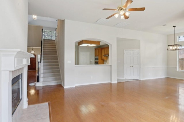 unfurnished living room featuring wood finished floors, ceiling fan, arched walkways, a fireplace, and baseboards
