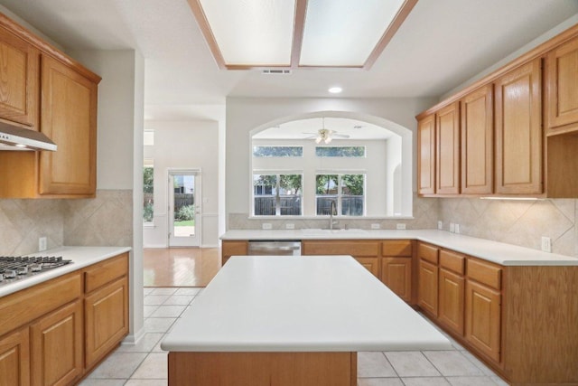 kitchen with a sink, stainless steel appliances, light countertops, a ceiling fan, and a kitchen island