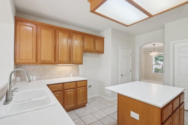 kitchen featuring a sink, arched walkways, tasteful backsplash, light countertops, and brown cabinetry