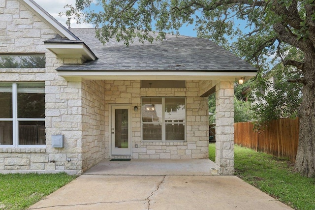 view of exterior entry featuring a shingled roof, stone siding, and fence