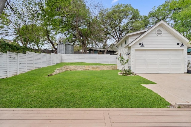 view of yard with a garage, a fenced backyard, and concrete driveway