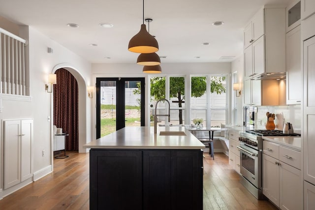 kitchen featuring light countertops, a sink, stainless steel range, a center island with sink, and light wood-style floors