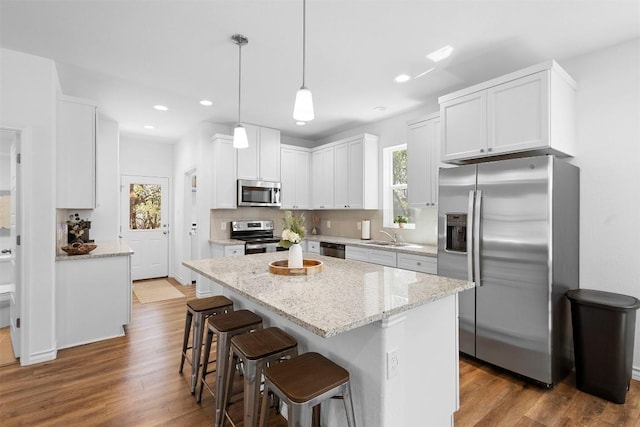 kitchen featuring white cabinetry, tasteful backsplash, wood finished floors, light stone countertops, and appliances with stainless steel finishes