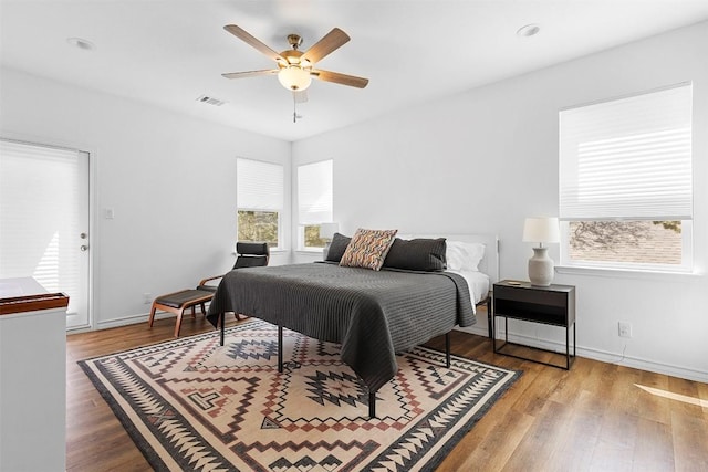 bedroom with multiple windows, visible vents, wood finished floors, and baseboards