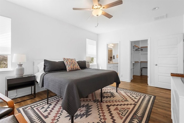 bedroom with a walk in closet, ensuite bath, ceiling fan, visible vents, and wood finished floors