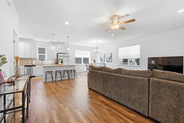 living room featuring ceiling fan with notable chandelier, visible vents, wood finished floors, and recessed lighting