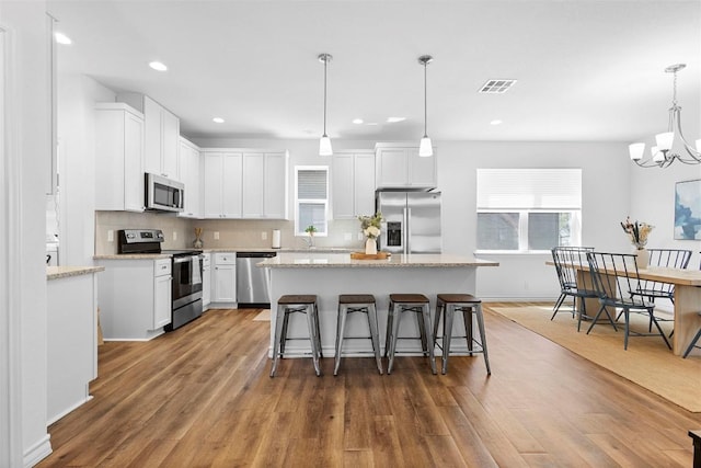 kitchen with white cabinets, wood finished floors, stainless steel appliances, a kitchen island, and a kitchen breakfast bar