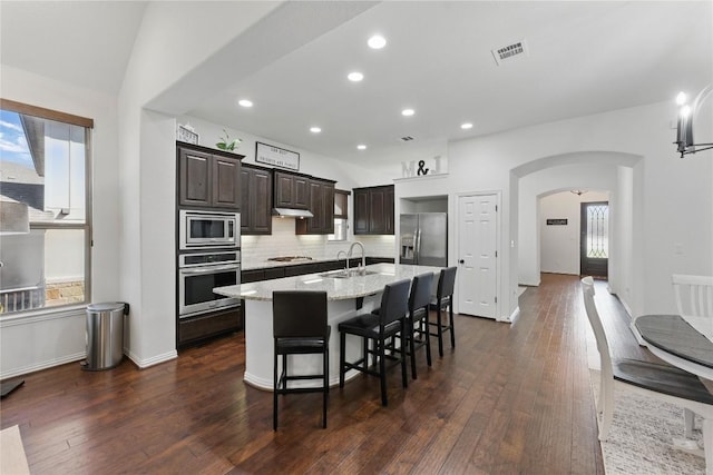 22300 Verbena Pkwy, Spicewood, TX 78669 - kitchen with stainless steel appliances, arched walkways, dark brown cabinets, an island with sink, and a breakfast bar