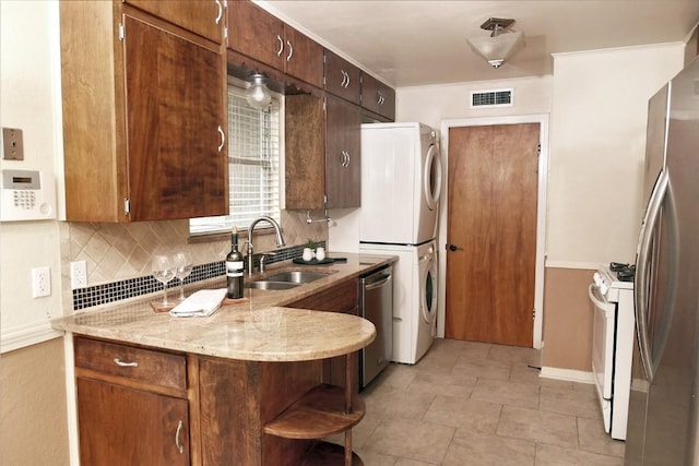 1410 Yorkshire Dr, Austin, TX 78723 - kitchen featuring appliances with stainless steel finishes, stacked washing machine and dryer, backsplash, light stone countertops, and a peninsula