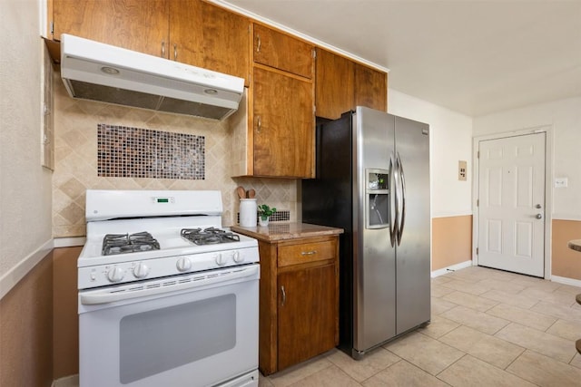 1410 Yorkshire Dr, Austin, TX 78723 - kitchen featuring white gas range, stainless steel fridge, under cabinet range hood, decorative backsplash, and brown cabinetry