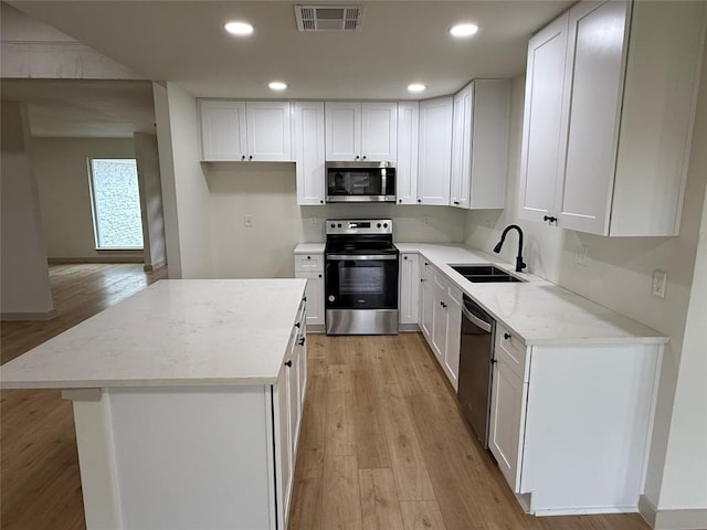 1402 Cardinal Hill Dr, Austin, TX 78758 - kitchen featuring appliances with stainless steel finishes, a sink, light wood finished floors, a kitchen island, and recessed lighting