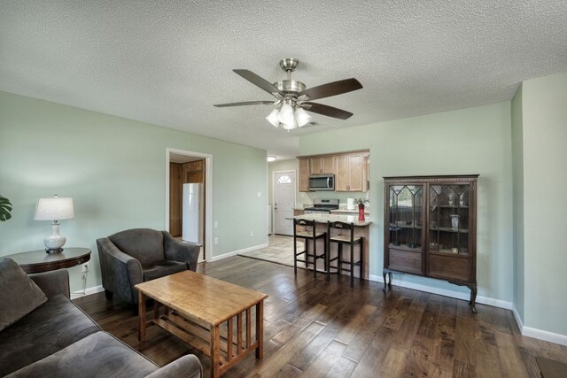 818 Kimbro St, Taylor, TX 76574 - living area featuring ceiling fan, dark wood-style floors, baseboards, and a textured ceiling