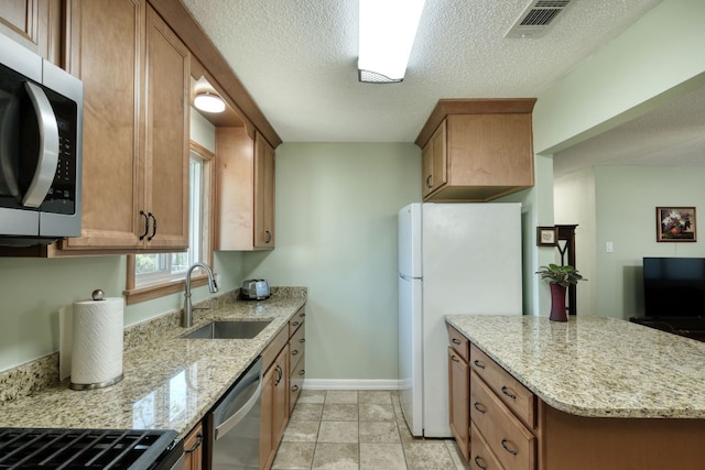 818 Kimbro St, Taylor, TX 76574 - kitchen with appliances with stainless steel finishes, a sink, light stone counters, brown cabinets, and a textured ceiling