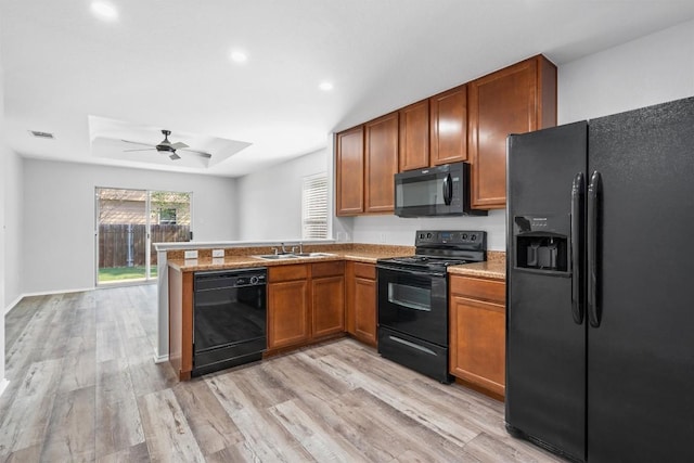 132 Grazing Horse Ln, Manchaca, TX 78652 - kitchen with light wood-style flooring, a peninsula, a raised ceiling, a sink, and black appliances