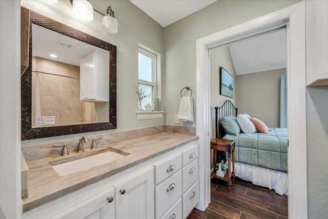 ensuite bathroom featuring wood finished floors, vanity, and tiled shower