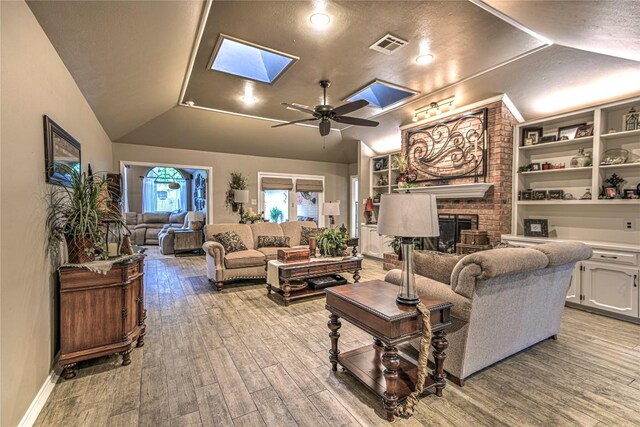 2921 Olympia Dr, Temple, TX 76502 - living room featuring visible vents, a fireplace, wood finished floors, ceiling fan, and vaulted ceiling with skylight