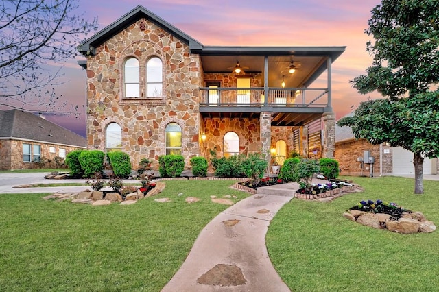 view of front of property featuring a lawn, ceiling fan, a balcony, and stone siding