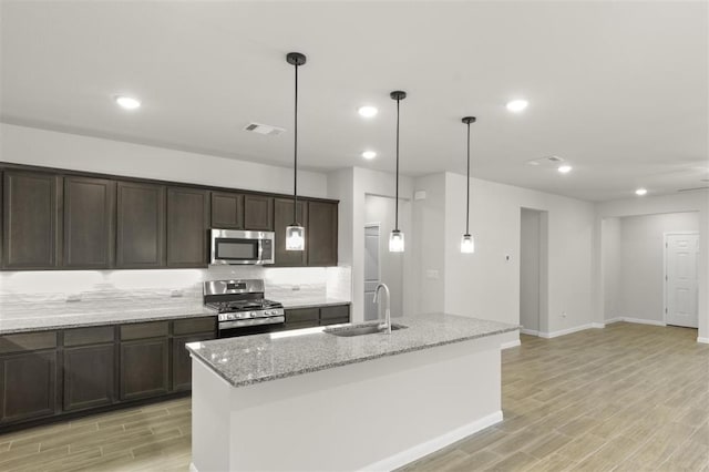 18309 Emu Ln, Manor, TX 78653 - kitchen featuring appliances with stainless steel finishes, a sink, light wood-style floors, light stone countertops, and dark brown cabinets